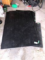 Three black rubber workout mats stacked with visible green tags and corner cut out on one mat.