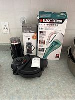 Oster waffle maker, Nespresso milk frother, Happy Time French press, Black & Decker Dustbuster cordless wet/dry hand vac on countertop with box.