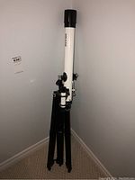 Full view of white Meade telescope tube mounted on black tripod against beige wall.