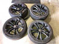 Four black Audi alloy wheels fitted with Maxtour LX tires arranged on garage floor, steering wheel cover at center.