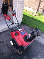Front angled view of the red and black Toro snowblower showing the handlebar, wheels, chute, and electric start engine compartment.