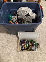Large blue plastic bin with a grey spaceship toy resembling the Millennium Falcon and various toy figures inside it, photographed from above with the bin open.