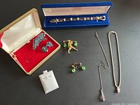 Overview of all lot items arranged on black surface including brooches, earrings, necklaces, bracelet box and stud display