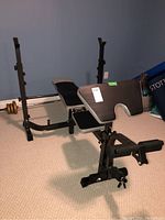 Weight exercise bench with adjustable backrest and leg extension attachment in a basement room with blue walls and carpeted floor
