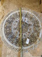 Photo of round area rug with measuring tape showing diameter approximately 31 inches, floral pattern, and fringe edge visible.