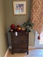 Full view of Asian style wooden cabinet with various decorative items on top and framed art on wall above.