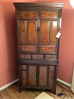 Full view of the tall Asian style wooden cabinet showing upper and lower compartments with inlaid wood panels and decorative metal hardware.