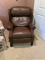 Front view of brown leather reclining chair showing wingback and studded armrests.