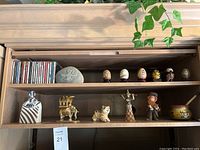 Long view of wooden cabinet shelves with various decorative collectibles including carved stone, painted eggs, ceramic figurines, and pottery items.