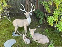 Photo showing set of four deer sculptures in outdoor garden setting on mossy ground near trees and bushes