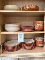 Detailed photo of assembled Denby dish set inside wooden cabinet with mix of bowls and plates in orange and cream colors