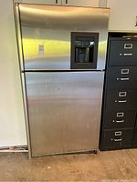 Full view of the stainless steel GE Profile refrigerator with top freezer and dispenser on front door.