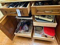 Photo showing two wooden drawers and two pull-out trays in kitchen cabinetry containing assorted kitchen utensils and items including knives, whisks, and other gadgets.
