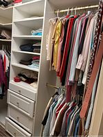 Wide angle shot showing hanging clothes on gold rods, shelves with folded clothes, and shoe boxes on upper ledges of the closet.