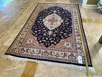 Full view of rectangular Persian-style area rug on marble floor with entry threshold at top. Tape measure placed along long side showing approximate length.