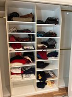 Full view of white shelving unit with multiple purses, handbags, and folded clothing items