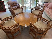 Round wooden coffee table surrounded by four bamboo-style armchairs with beige cushions in a living room setting.