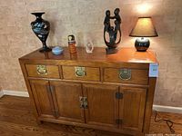 Front view of Century Sobota Collection wooden sideboard with three drawers and four doors, displaying decorative items on top including vases, sculptures, and lamp.