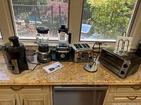 Wide photo of countertop with all small kitchen appliances including juicer, two blenders, toaster, oven toaster and toast rack.