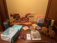 Full lot overview showing dragon sculpture, crystal bowl box, wooden elephants, calculator, Swiss knives, cups and coasters.