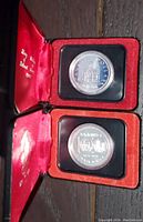 Two silver dollar coins displayed in open presentation cases showing the front design of the 1976 Parliament Library coin and the reverse of the 1974 Winnipeg coin.