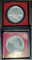 Coin encapsulated in original black display case with red interior lining and Olympic rings logo visible.