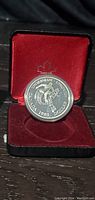 Front side of silver proof coin showing hockey player and inscriptions inside red velvet-lined case with maple leaf emblem on lid.