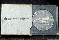 Image depicting the 1984 Canadian Silver Dollar coin in a clear plastic case alongside its white cardboard box featuring the Royal Canadian Mint logo and bilingual text.