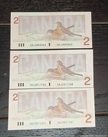 Three 1986 Canadian $2 bills arranged horizontally showing the front side with bird illustrations and consecutive serial numbers.