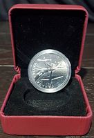 Front side of the coin showing the early biplane and compass design, inside a red display box with black velvet interior.