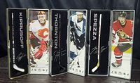 Front view showing three mini hockey sticks in display cases with player images and names: Kiprusoff, Thornton, Spenza.