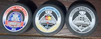 All three pucks side by side showing front designs: Official Game Puck in red/white/blue, Championship puck with gold emblem, and Practice puck in black/white.