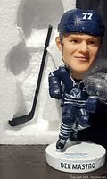Front view of Ethan Del Mastro bobble head with visible facial features and hockey stick beside it.