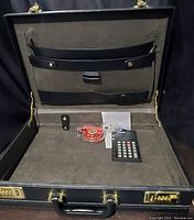 Open vintage Bugatti black leather briefcase showing interior compartments and items inside including calculator, tape dispenser, and measuring tape