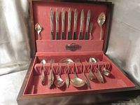 Opened wood case showing arranged silverplate flatware set inside with red velvet lining.