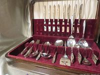 Complete silverware set neatly arranged inside red velvet-lined wooden case, showing forks, knives, spoons, and specialty serving pieces.