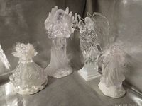 Four angel figurines: two clear crystal glass angels including a multi-color LED light angel, and two resin angels with feather and flower decorations