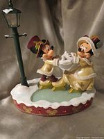 Front view of Victorian Mickey and Minnie skating figure statue with lighted base and street lamp.