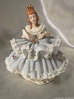Front view of Dresden porcelain figurine showing lady in ruffled blue dress holding a fan, detailed lace trim, and golden crown.