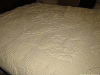 Full view of the king size quilt spread out on bed showcasing detailed floral and feather trapunto designs with matching pillow sham folded on top.