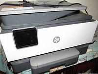 Front and top view of the HP Officejet 9018e All-in-One Printer showing the power cord, touchscreen, and scanner lid.