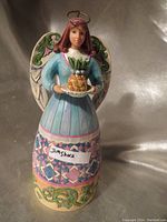 Front view of the Jim Shore Heartwood Creek angel figurine holding a pineapple on a plate, showcasing detailed painting and colors.