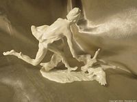 Side view of bisque porcelain statue showing man kneeling and reaching towards two geese extending wings, detailed base visible.