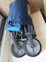 Folded pet wagon showing large wheels and metal frame partially covered in dark fabric.