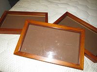 Three wooden shadow boxes stacked on a surface, showing the closed glass fronts and warm wood frames.