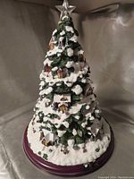 Front angled view of triangular Christmas tree village featuring lit star on top and snow-covered miniature buildings and figurines.