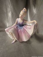Front view of Royal Doulton Dancing Years figurine in a ladylike pose with flowing purple-pink dress and blonde hair tied with pink ribbon.