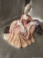 Front view of Royal Doulton 'Reverie' porcelain figurine depicting seated woman in pink gown holding a book on a chaise lounge.