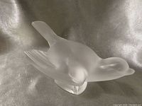 Side view of frosted clear Lalique crystal sparrow sculpture showing wing and body details on a reflective surface.