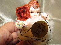 Close-up front view of the Simpich Cloud Baby doll holding a small brown teddy bear, showing facial features and attached branding tag with string.